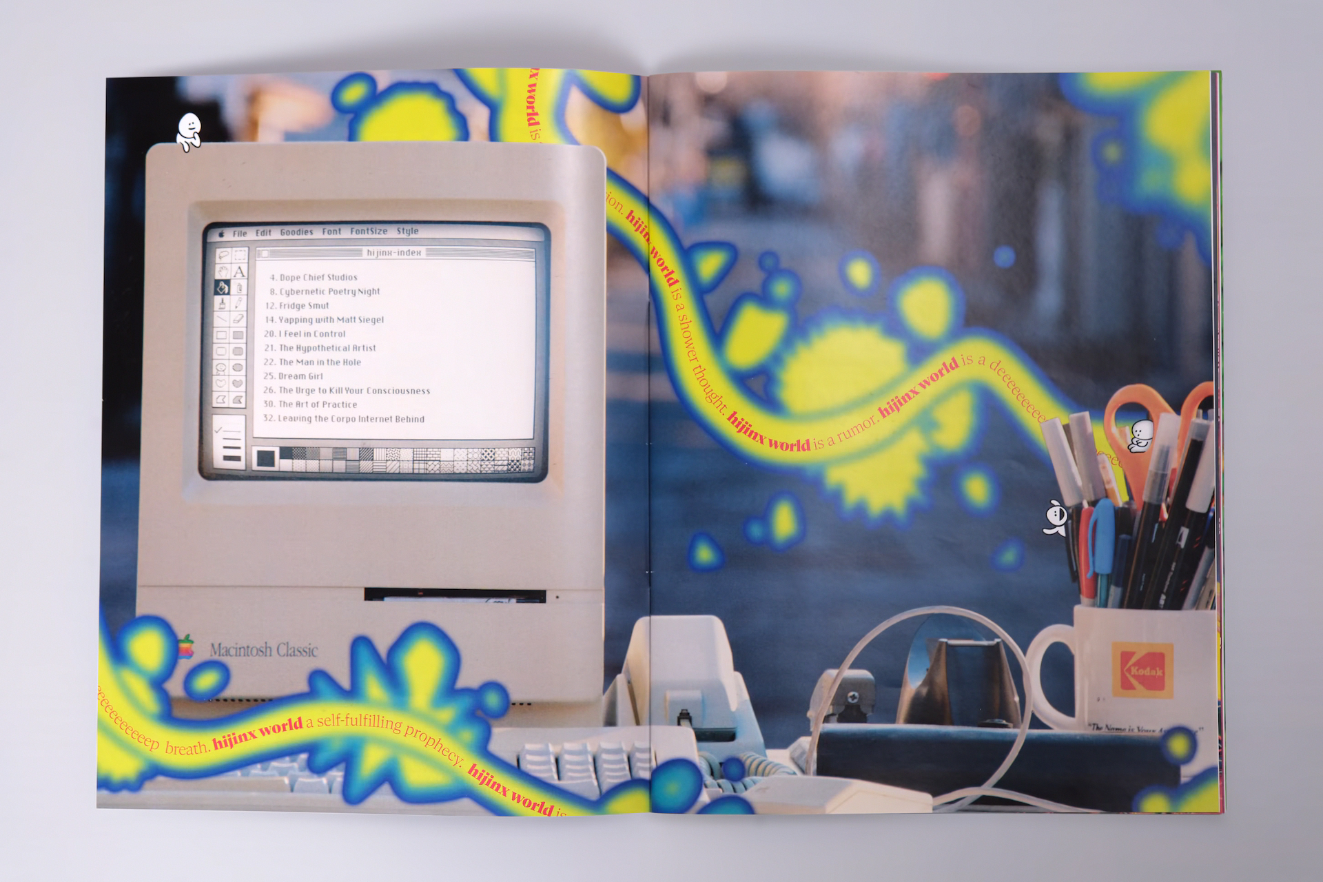 Magazine spread of a Macintosh Classic sitting atop a desk in an alleyway. The Macintosh has the table of contents displayed on the screen in MacPaint